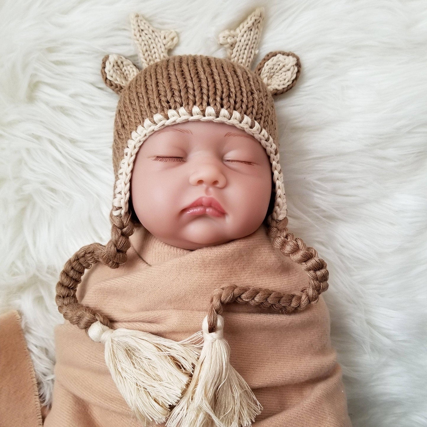 Baby wearing knitted deer hat with antlers and tassels, wrapped in soft blanket