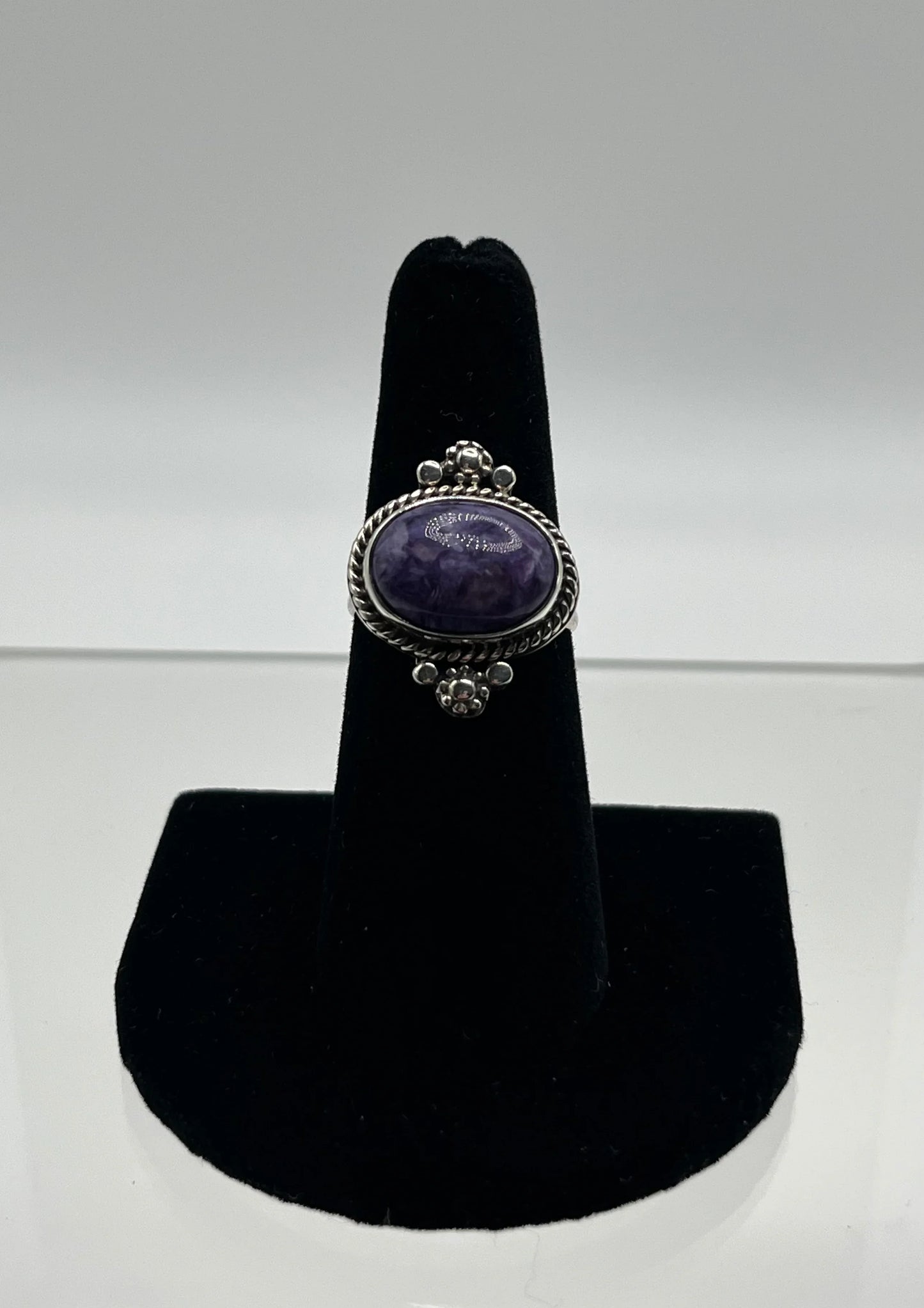 Amethyst silver ring with rope border and bead accents, displayed on black stand