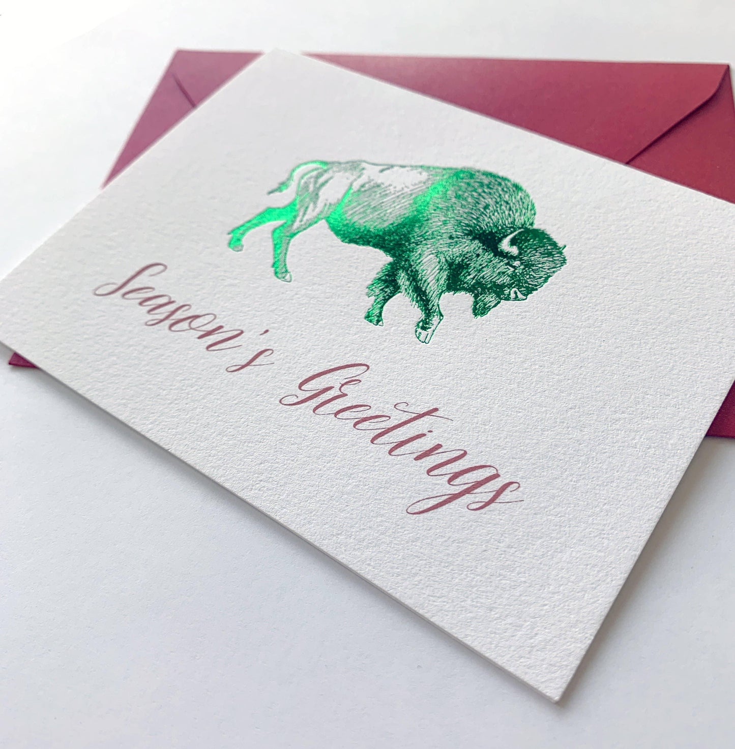 Season's Greetings card with green bison illustration, festive holiday design, red envelope