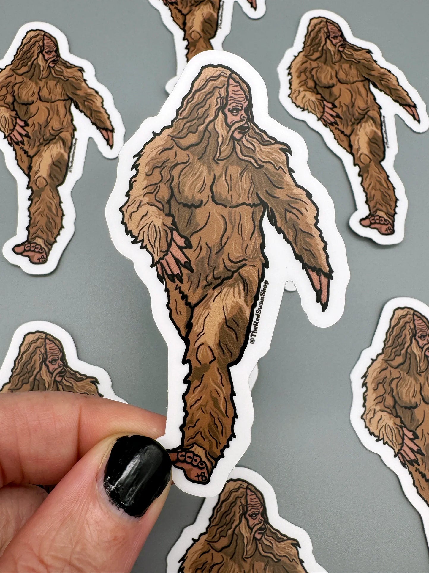 Bigfoot sticker with detailed fur, held against gray background with more stickers visible