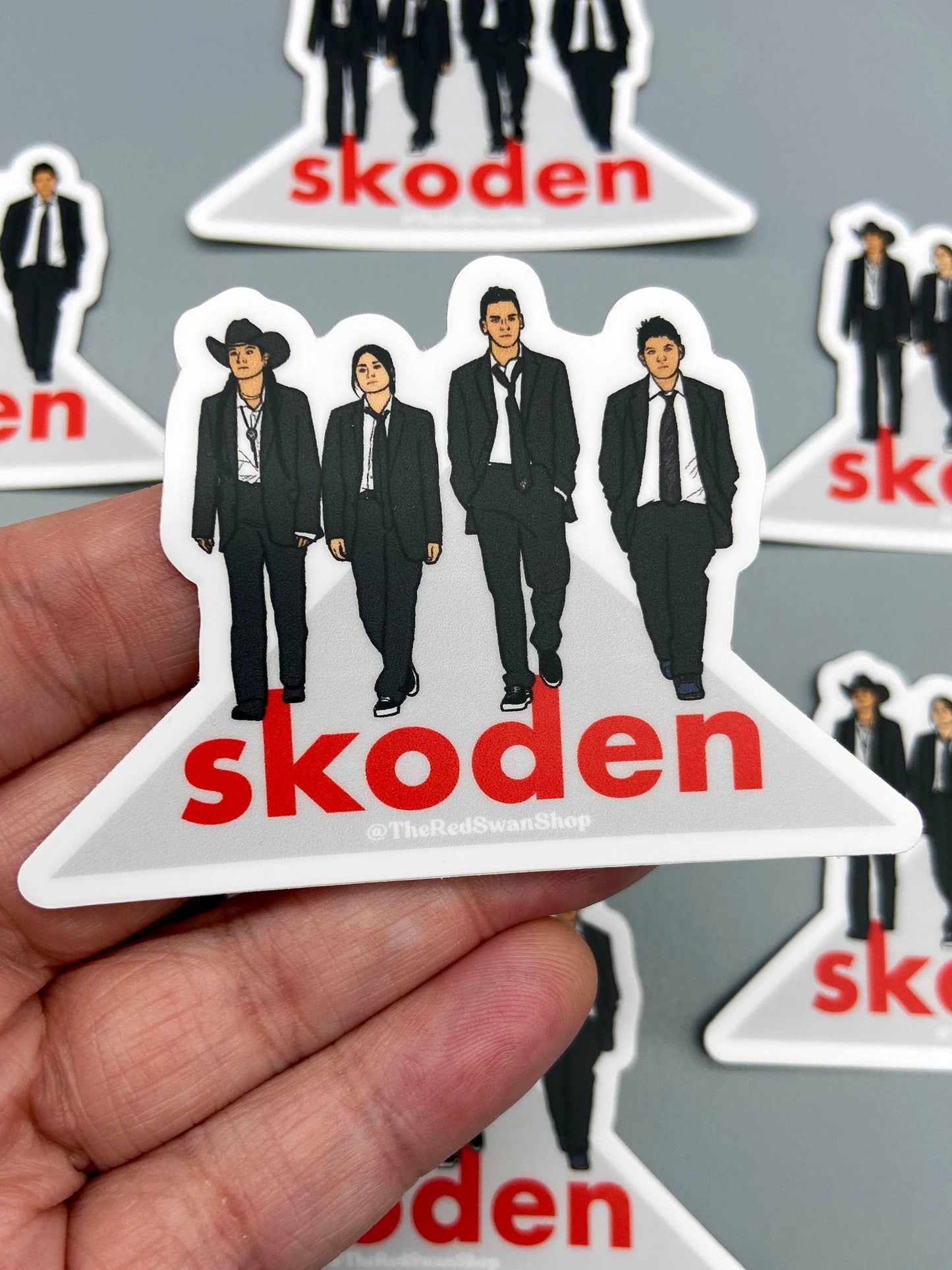 Skoden sticker featuring four figures in suits, one with a cowboy hat, held in hand