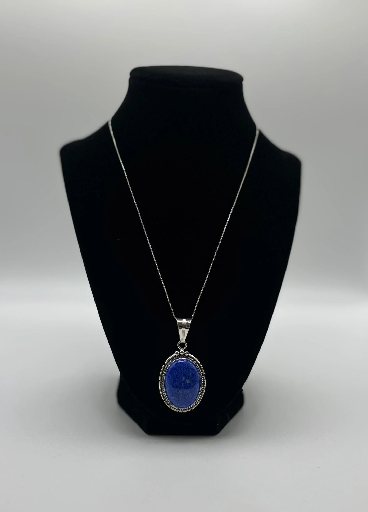 Oval lapis lazuli pendant necklace with silver chain, displayed on black velvet stand