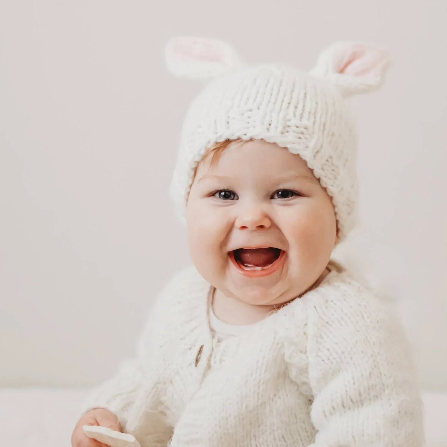 Happy baby wearing white knitted bunny hat and sweater, smiling brightly