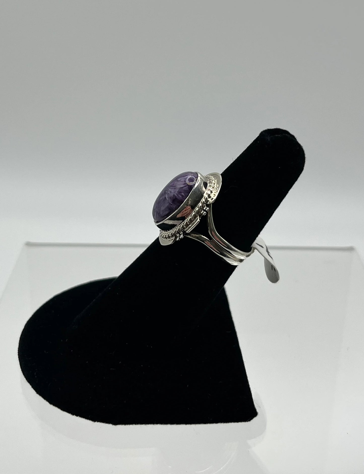 Purple stone silver ring with intricate metalwork, displayed on black velvet stand