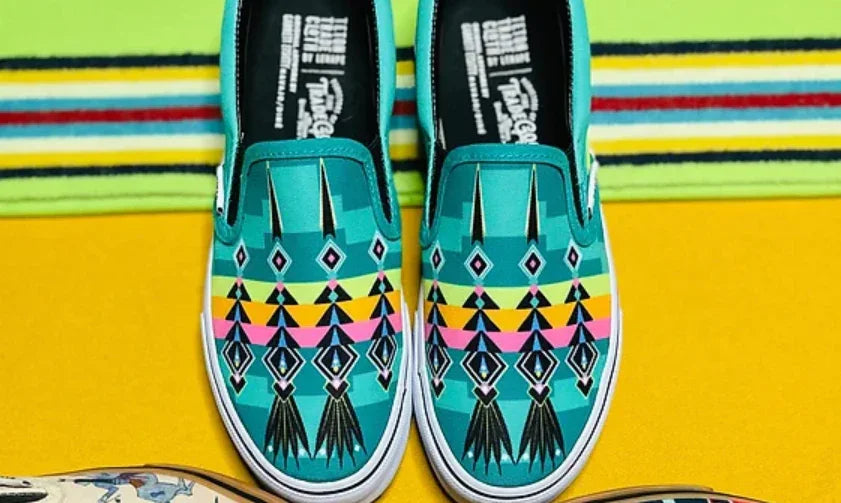 Teal slip-on shoes with Native-inspired geometric patterns on colorful striped background