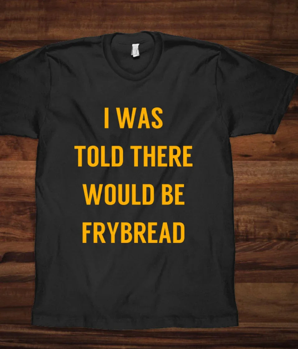 Black t-shirt with bold yellow text: 'I WAS TOLD THERE WOULD BE FRYBREAD' on wooden background