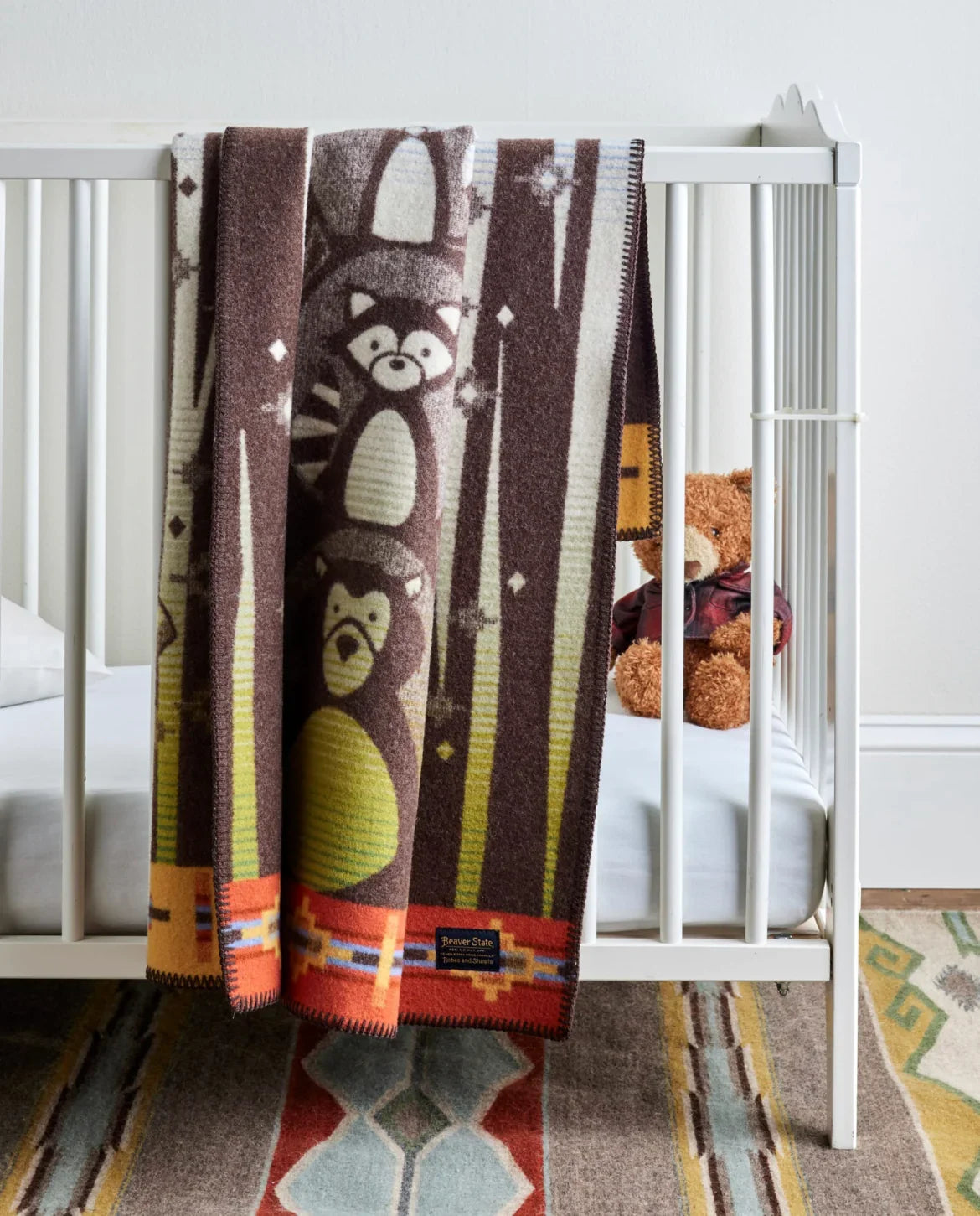 Native-inspired baby blanket with raccoon & bear design, draped over crib, tribal patterns, cozy nursery decor