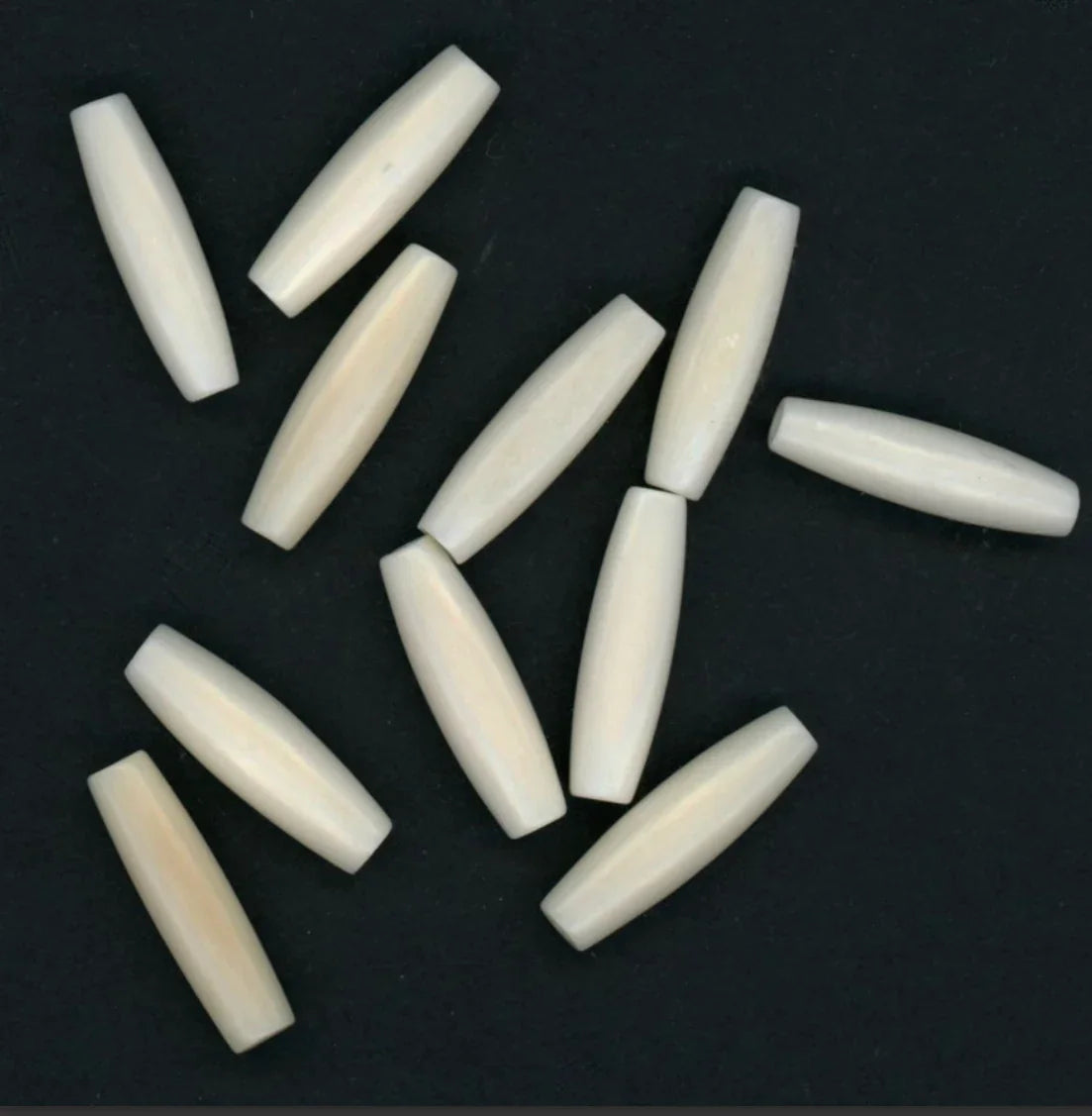 Ivory-colored bone beads for Native American craft and jewelry making, smooth oval shape on black background