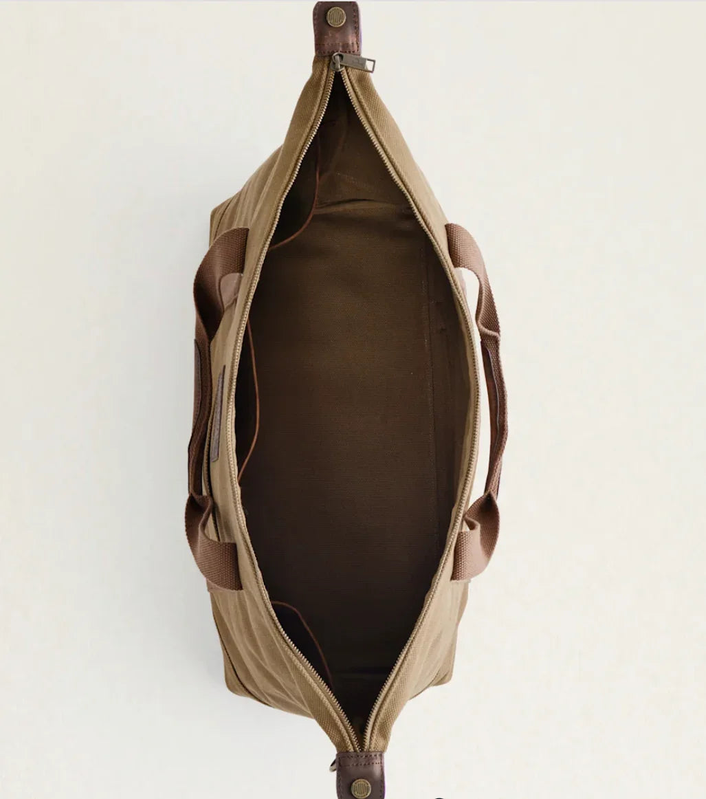 Tan canvas duffel bag with brown leather accents, open to show spacious interior for art supplies or travel gear
