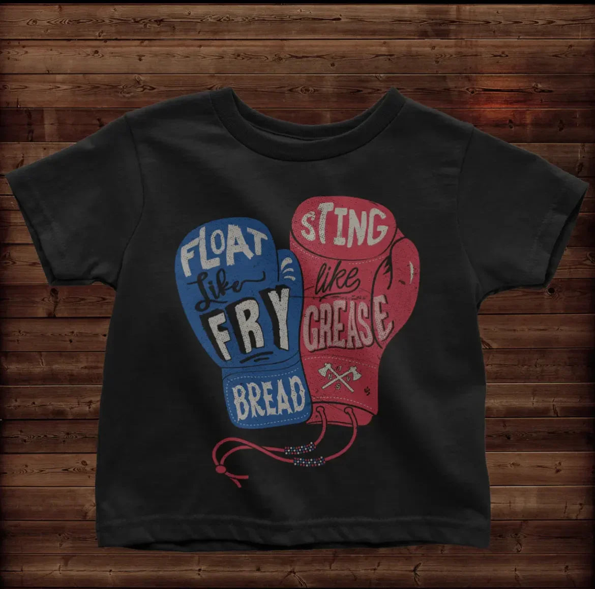 Black toddler tee with 'Float like Fry Bread, Sting like Grease' boxing gloves graphic on wood background
