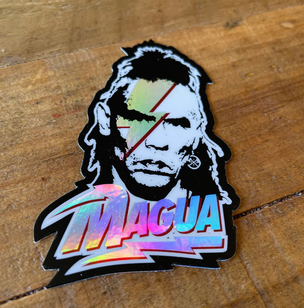 Holographic Magua sticker with bold graphic design on wooden surface
