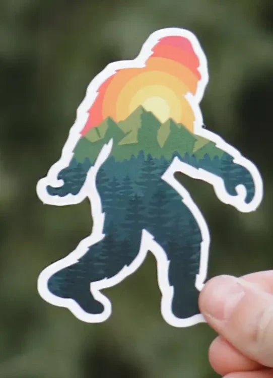 Rainbow sunset Bigfoot sticker with forest design, held in hand