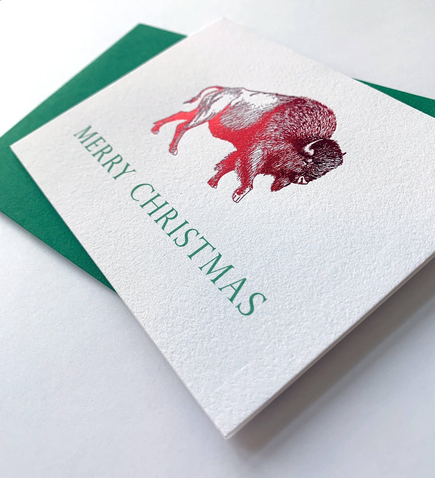 Merry Christmas card with red bison illustration, green text, and matching envelope