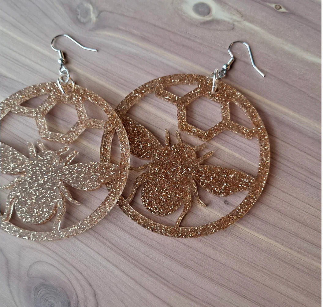 Glittery bee earrings with honeycomb design on wooden surface