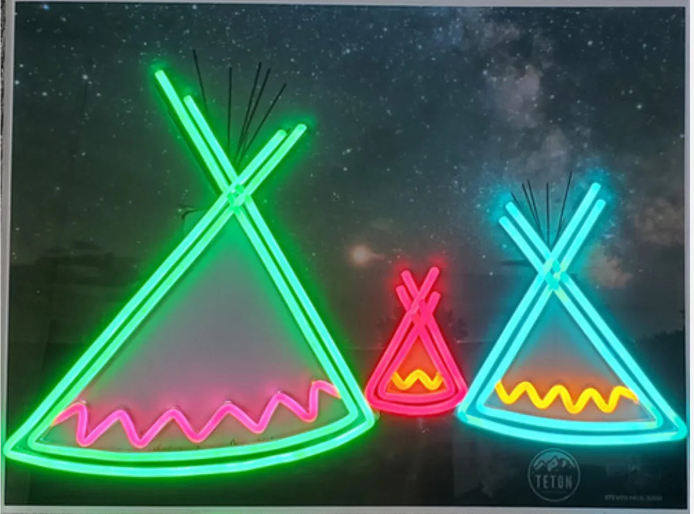 Neon teepee art with glowing green, pink, and blue designs against a starry night sky.