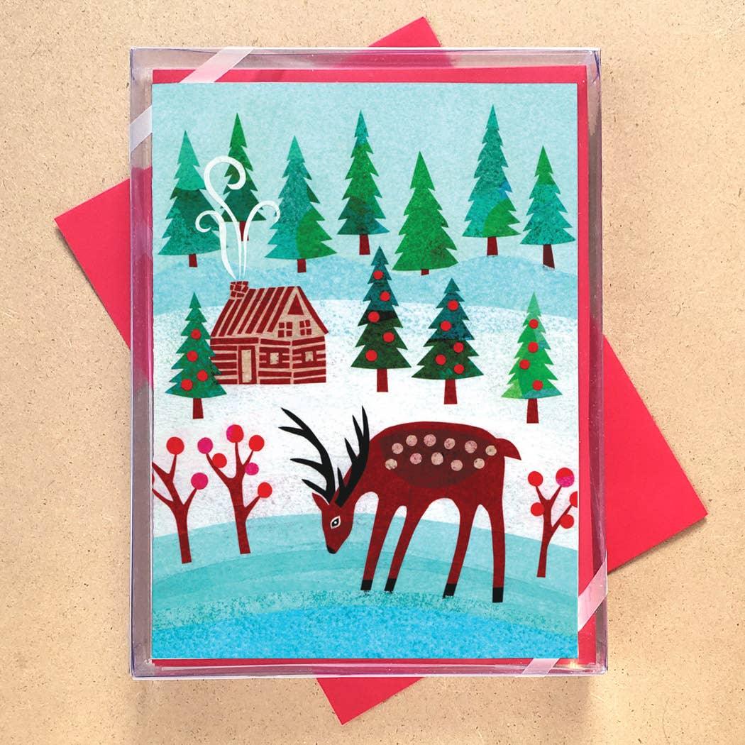 Winter cabin scene with deer, pine trees, and red berries on greeting card