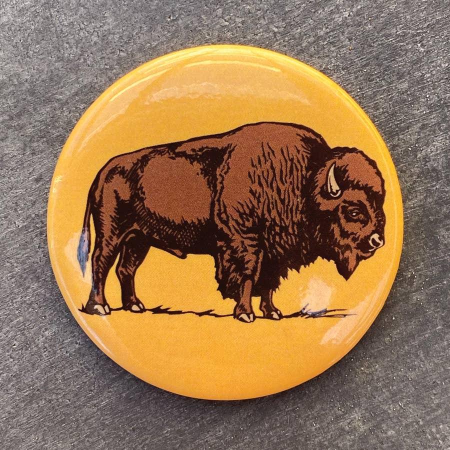 Yellow button featuring a detailed bison illustration, symbolizing Native American art and culture.
